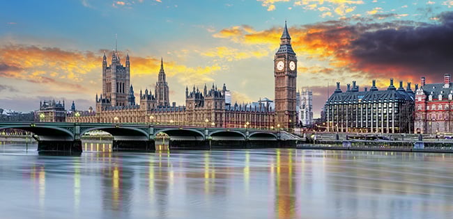 A stunning view of London, England, featuring the iconic Big Ben and the Houses of Parliament along the River Thames. Westminster Bridge spans the calm water, reflecting the warm colors of a dramatic sunset sky with hues of orange, yellow, and purple. The historic architecture and vibrant atmosphere capture the essence of the city.