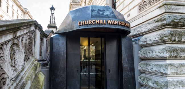 The entrance to the Churchill War Rooms, featuring a sleek, black modern canopy with the name prominently displayed in bold lettering, surrounded by historic stone architecture and ornate railings.