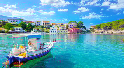 A vibrant coastal scene in Greece featuring a small fishing boat floating on crystal-clear turquoise water. In the background, colorful houses with bright facades line the shore, surrounded by lush greenery and rocky terrain. The sky is a brilliant blue with scattered white clouds, enhancing the idyllic Mediterranean atmosphere.