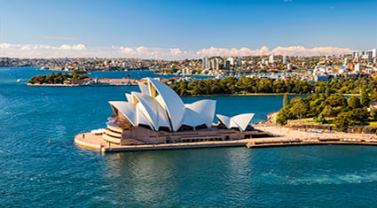 The iconic Sydney Opera House on the waterfront with the Sydney skyline in the background, bathed in golden sunlight.