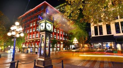 Night view of Vancouver’s historic Gastown district featuring the iconic steam clock, red-brick buildings, and tree-lined streets illuminated by streetlights.