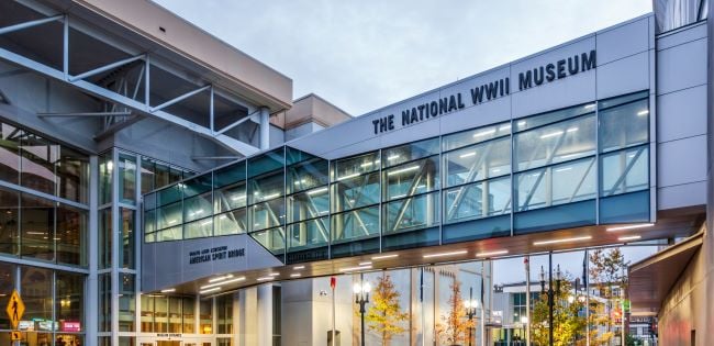 Exterior view of The National WWII Museum in New Orleans, featuring the American Spirit Bridge glass walkway connecting buildings at dusk.