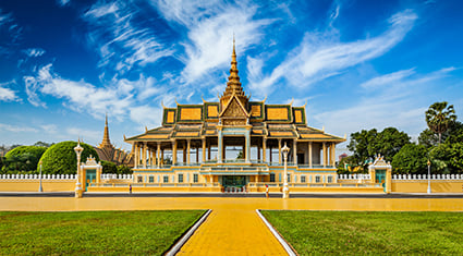 The Royal Palace in Phnom Penh, Cambodia, with its golden spires and symmetrical architecture framed by vibrant green lawns and a bright blue sky.