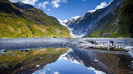 A clear mountain river flows through a valley surrounded by snowcapped peaks and forested slopes on New Zealand’s South Island.