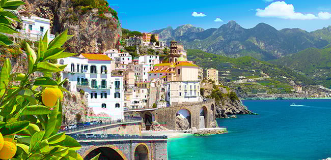 The coastal village of Atrani on Italy’s Amalfi Coast, with pastel buildings stacked on cliffs above the turquoise sea, framed by lemon trees.