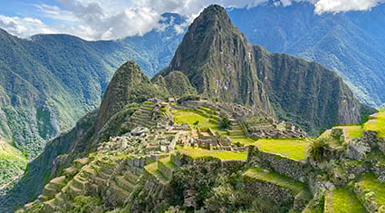 The ancient Incan citadel of Machu Picchu in Peru, perched on a mountain ridge with surrounding peaks and lush green terraces.