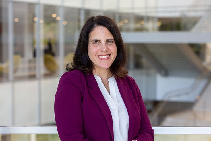 Laurel Ofstein, faculty advisor, poses in wine-red blazer and white blouse with the Minskoff Pavilion in background