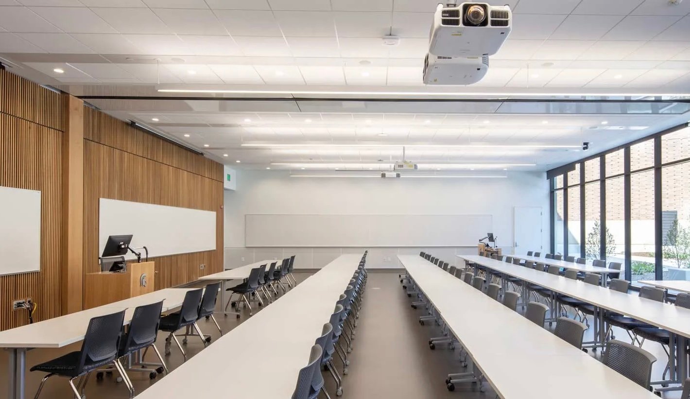 Bright room with long tables and chairs, natural sunlight, and large whiteboards.