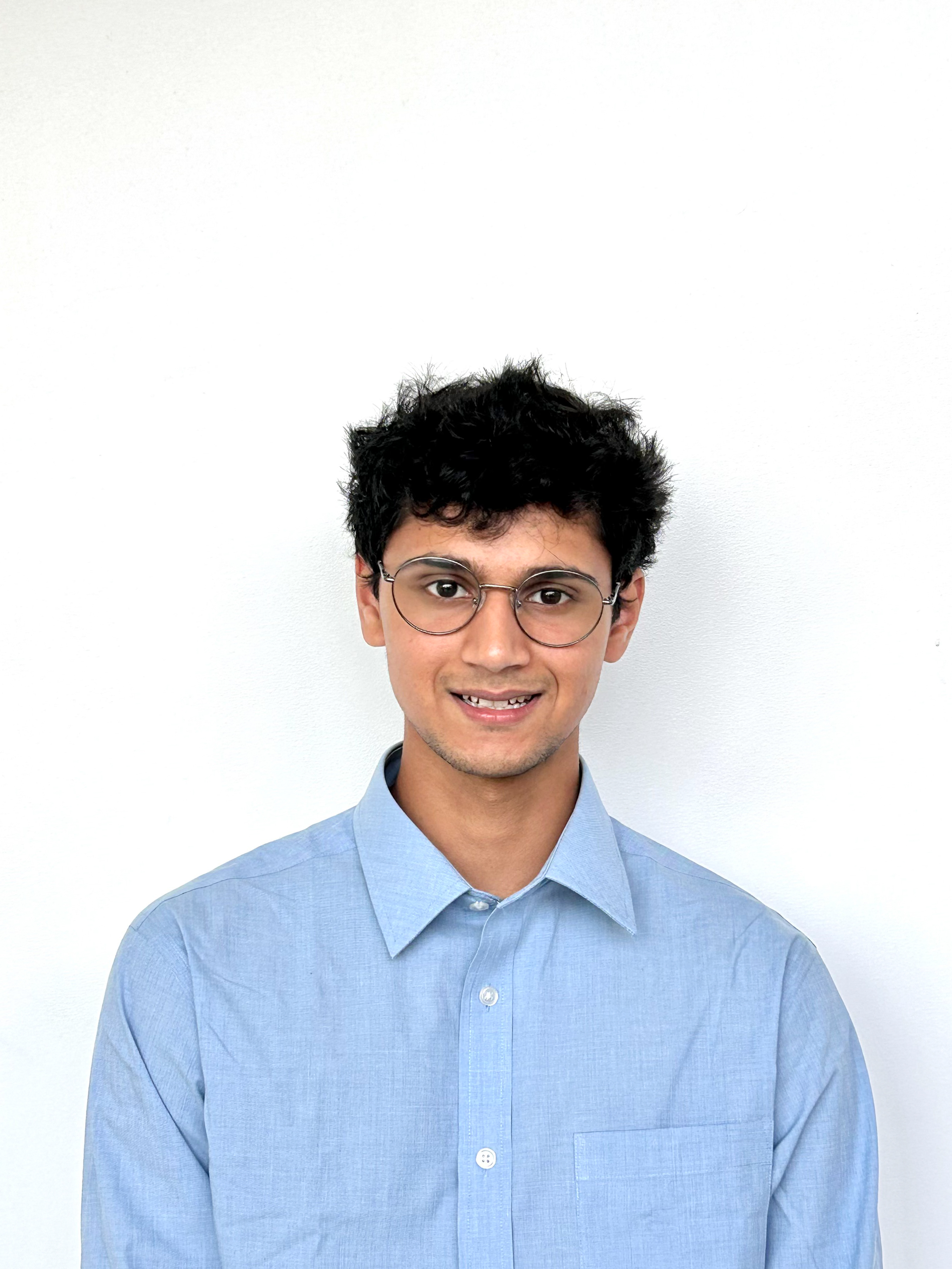 Ashu Lodd poses in a blue button-down dress shirt and round glasses.