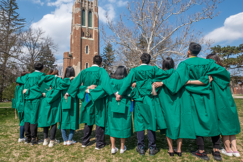Students arm-in-arm in front of Beaumont Tower in their graduation gowns. 