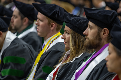 Graduating students viewing commencement speaker at their graduation ceremony.