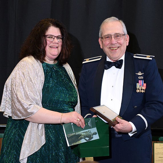 Geoff Gavrila in a veteran?s uniform holding an award next to Laura Genik.