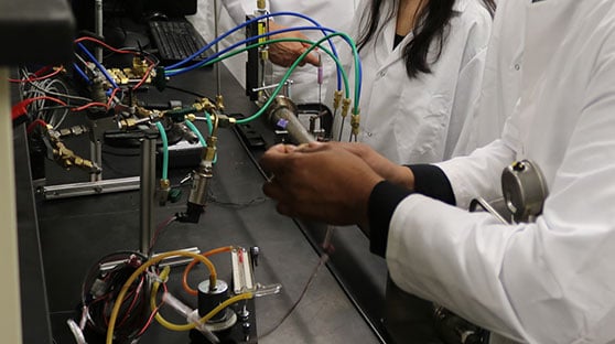 Students in lab coats and handling lab equipment with a lot of wires