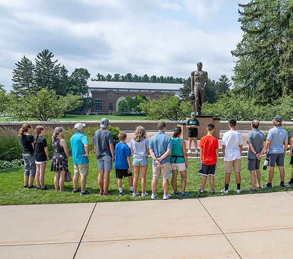 Campus Tour guide and tour participants in front of the Spartan Statue on a sunny summer day.