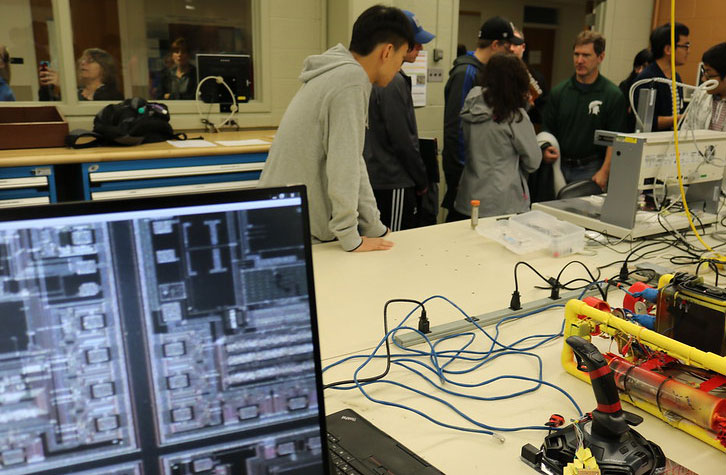 close up of a computer and wires with students during Engineering Preview Day in the background