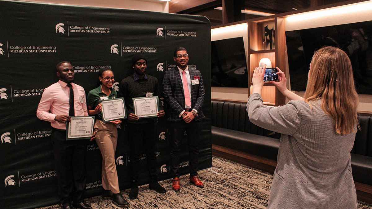 Students holding their awards while someone from the company is taking a photo of them with their phone