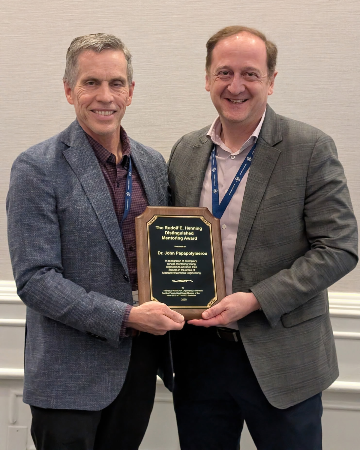 Two men standing side-by-side hold an award between them