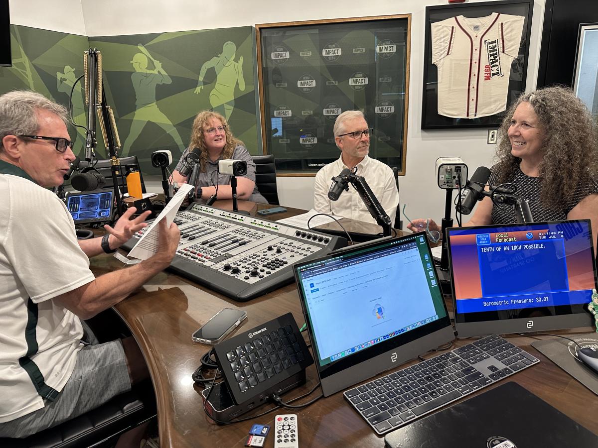 4 people sitting around a desk in front of microphones