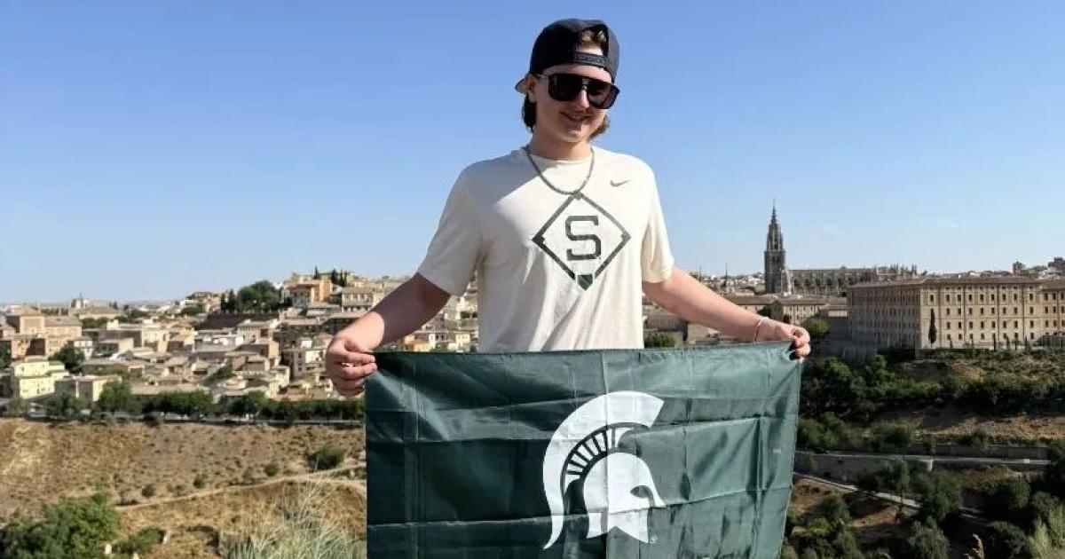 Student Adam Sargent stands with a green and white MSU flag and a Spain landscape in the background.