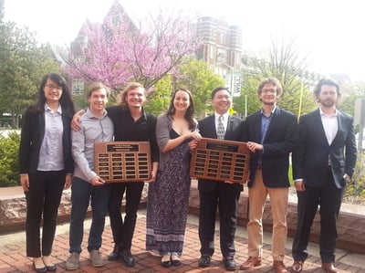Undergraduates smiling and holding two awards plaques with their names on them. 