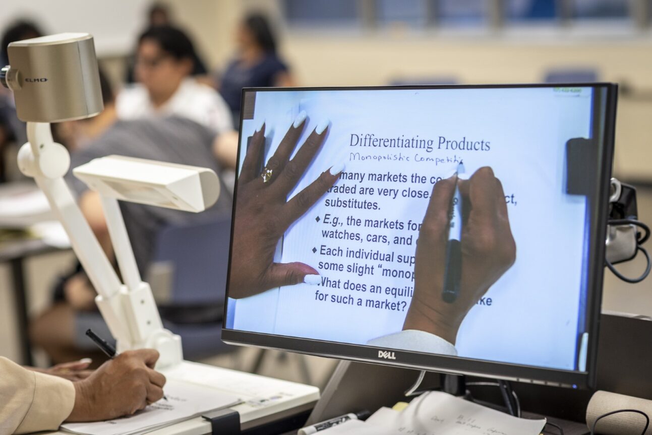 A professor writes on a projector screen. 