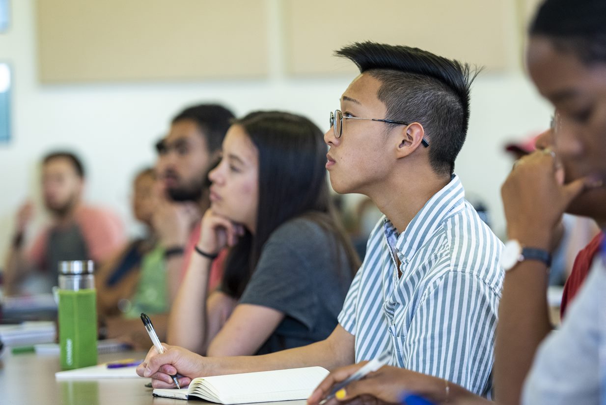 A row of students taking notes in a classroom.
