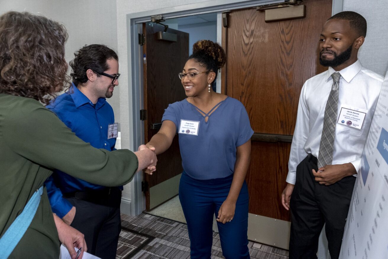 A black woman shakes hands with a white woman while a black man and white man stand in their cirlce.