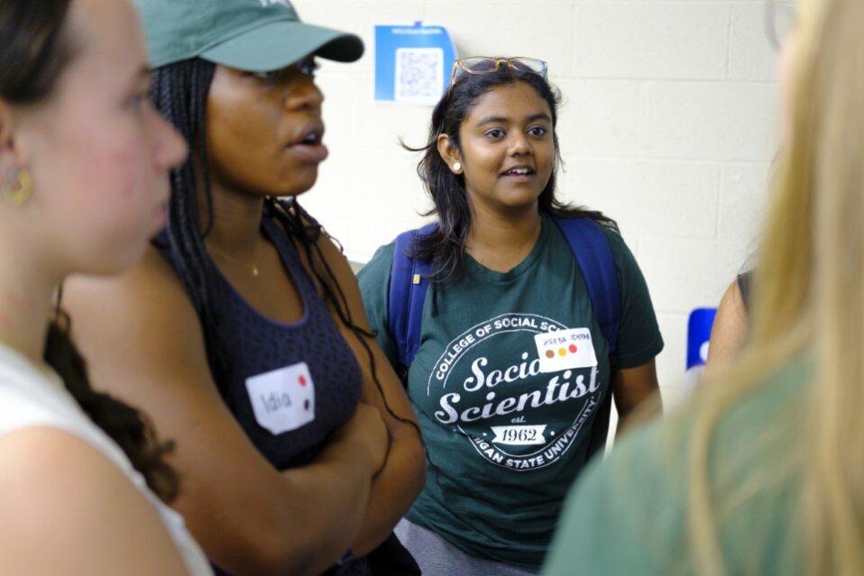 One South Asian female student wearing a t-shirt that says social science talks to a black female student and two white female students.