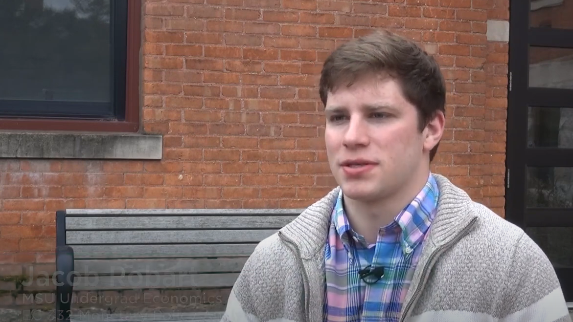 Male MSU graduate speaks outside a brick building. 