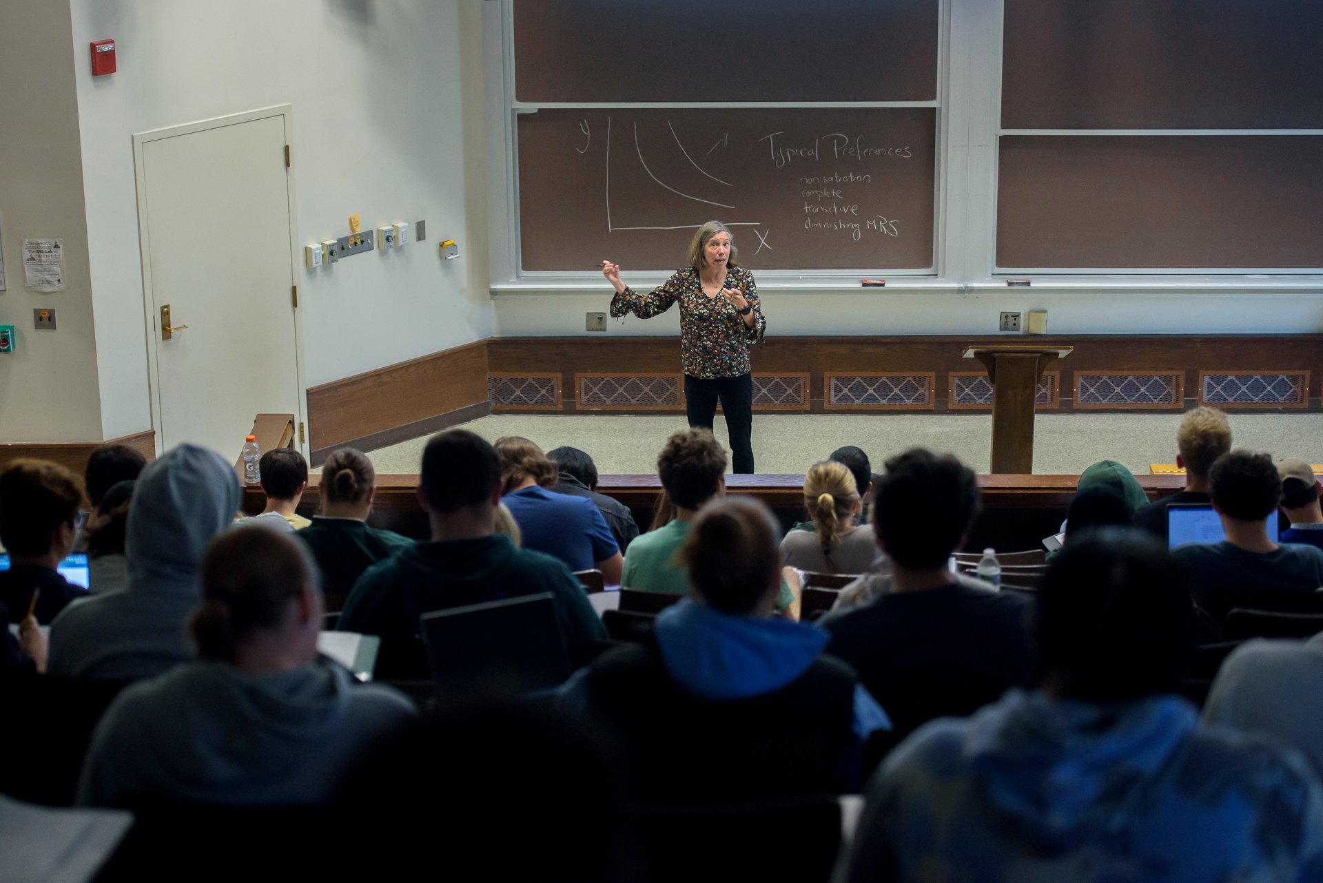 Professor describes concept on board to lecture hall of students.