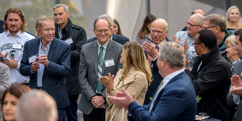 Dr. Jeff Wooldridge smiles while colleagues who surround him clap for him. 