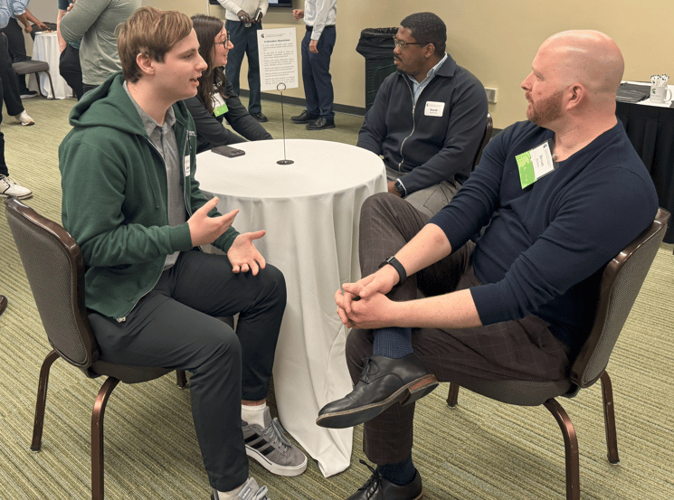 Two alumni members speak with two students.