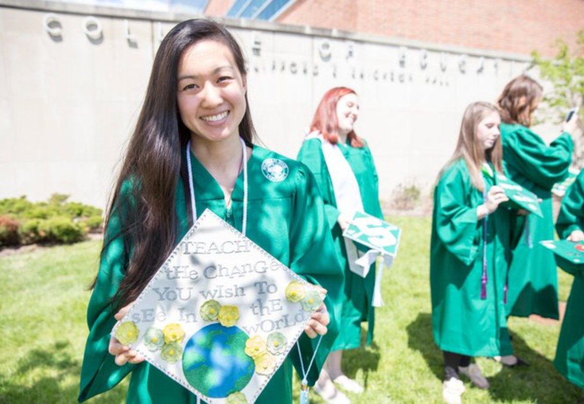 Spartan student holding graduation cap that reads "teach the change you wish to see in the world"