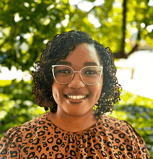 This is a photo of Madison. She has black curly hair that is just above her shoulders, is wearing glasses, and is smiling.