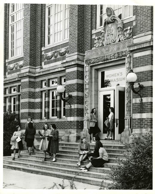 Historical photo of students sitting on the steps of a brick building.