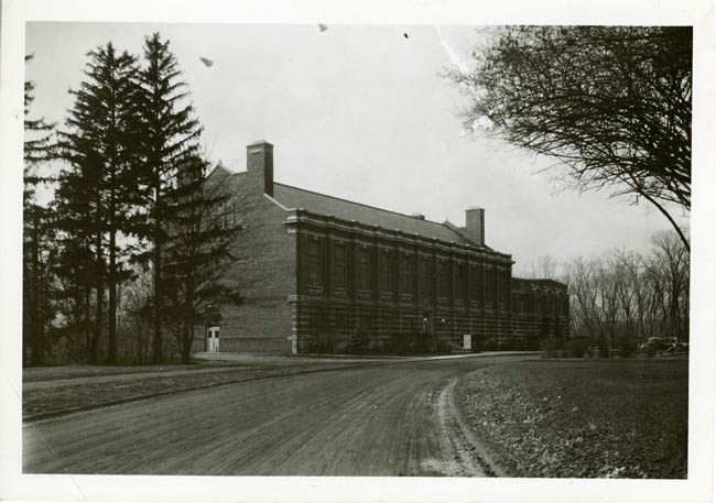Black-and-white photo of an old academic building with bare trees nearby.