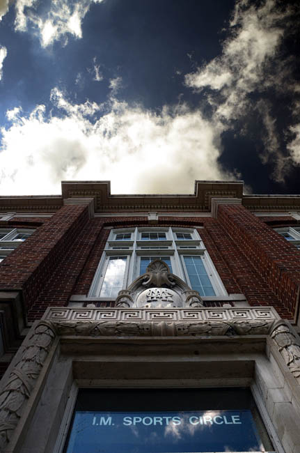 Upward view of the entrance to a historic building with "IM Sports Circle" engraved above.