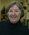 Color photo of a woman with short hair, wearing a dark turtleneck sweater and smiling brightly.