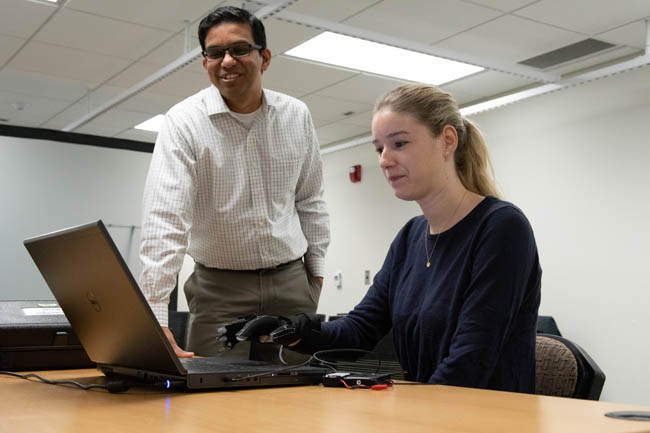A professor and student analyzing data on a laptop in a lab setting.