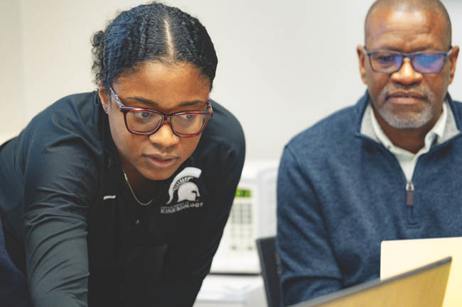Two researchers collaborating in a lab, one wearing an MSU Spartan shirt.