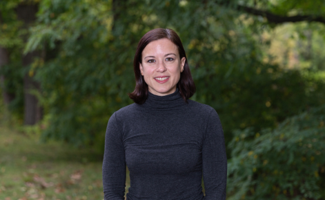 Adrea Truckenmiller stands outdoors smiling. She is wearing a long sleeve black top.
