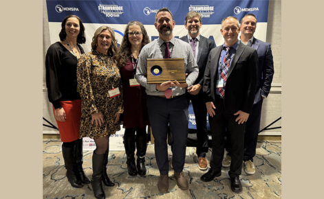 Cherry standing in center surrounding be peers. He is holding an award an everyone is smiling.