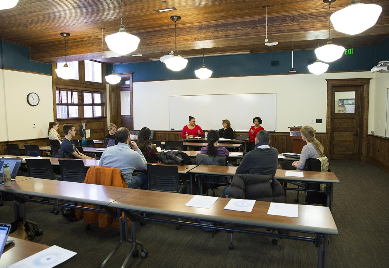 Scholars sit at the front of a classroom and lead a panel discussion