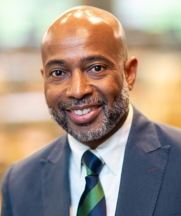 Jerlando Jackson headshot. He wears a dark gray blazer and a green and blue tie.