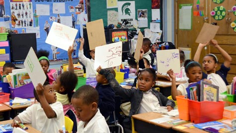 Students in a classroom raising their hands with papers