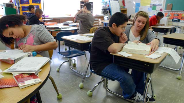 A teacher kneels by a desk to support a learner