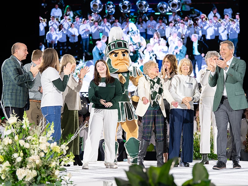 President Guskiewicz surrounded by students and alumni and Sparty on stage