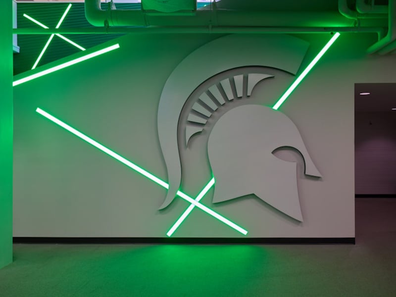 Large Spartan helmet wall art with glowing green light beams in a contemporary Michigan State University hallway.