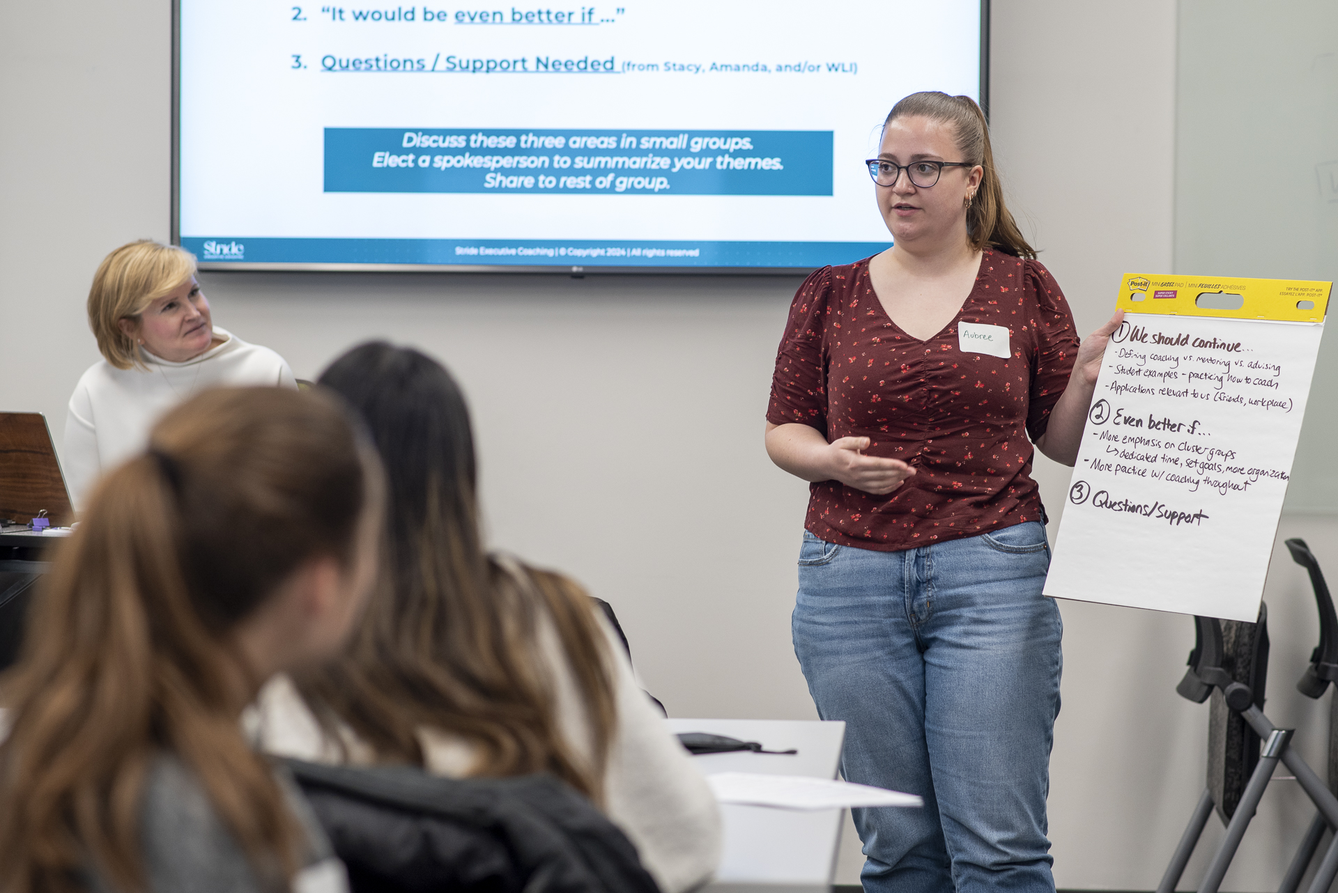 Woman at front of class presenting a poster to a group.