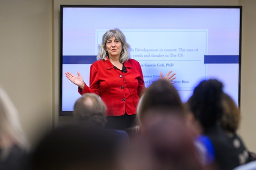 Dr. Garcia Coll talks to a crowd in front of a PowerPoint presentation.